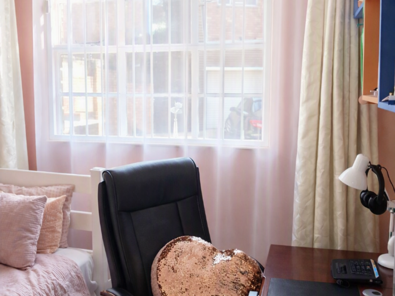 A bedroom featuring laminate flooring and a window fitted with security bars, providing natural light and a view of the exterior.