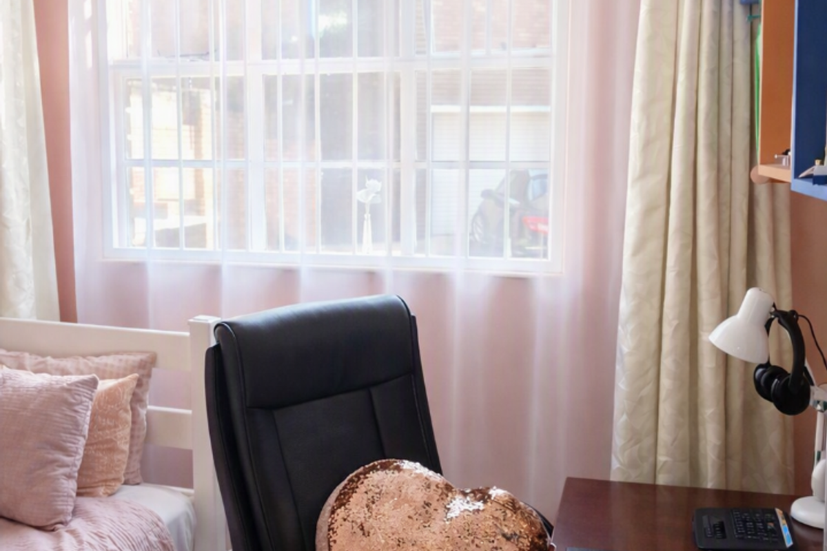 A bedroom featuring laminate flooring and a window fitted with security bars, providing natural light and a view of the exterior.