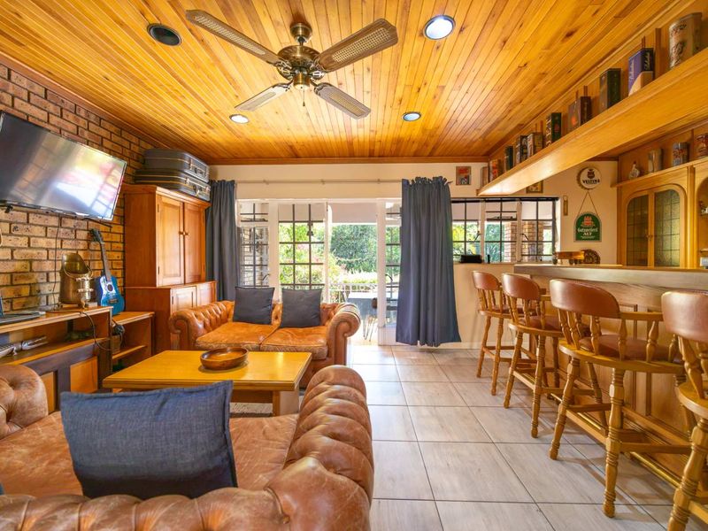 A cozy entertainment room featuring a built-in bar, exposed brick wall, warm timber ceiling, and direct access to the outdoor area through sliding doors.
