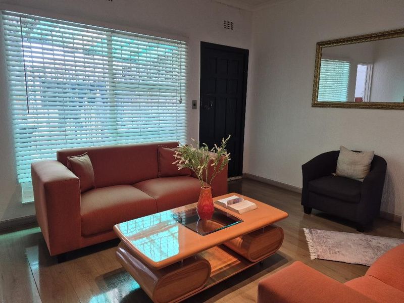 A comfortable living room featuring laminate flooring, coving, and large windows fitted with venetian blinds, providing a bright and functional space.