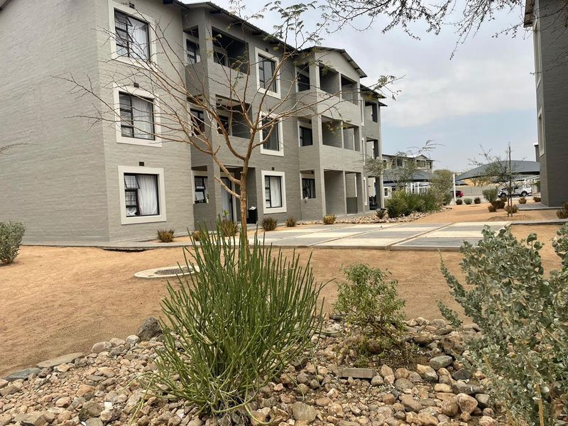 Exterior view of a multi-story apartment complex featuring modern grey facade, private balconies, and landscaped communal grounds.