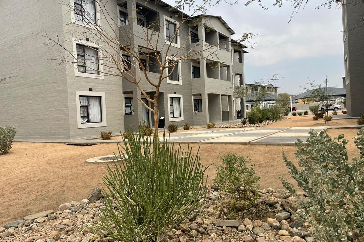 Exterior view of a multi-story apartment complex featuring modern grey facade, private balconies, and landscaped communal grounds.
