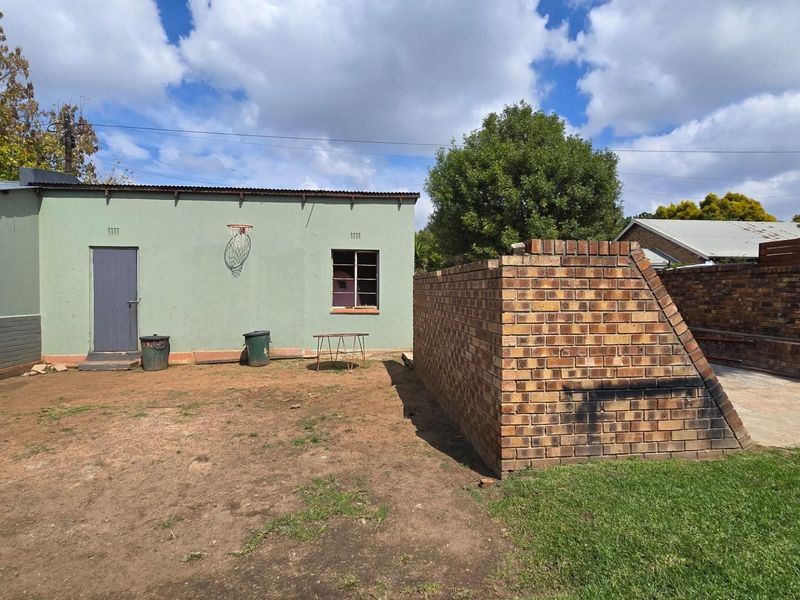 Rear exterior view featuring a brick boundary wall, built-in braai area, and concrete patio space in a garden setting.