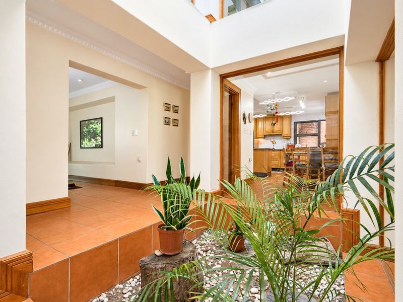 A bright, open-plan hallway featuring terracotta tiling, timber accents, and a central internal atrium, providing a unique architectural connection between living spaces.