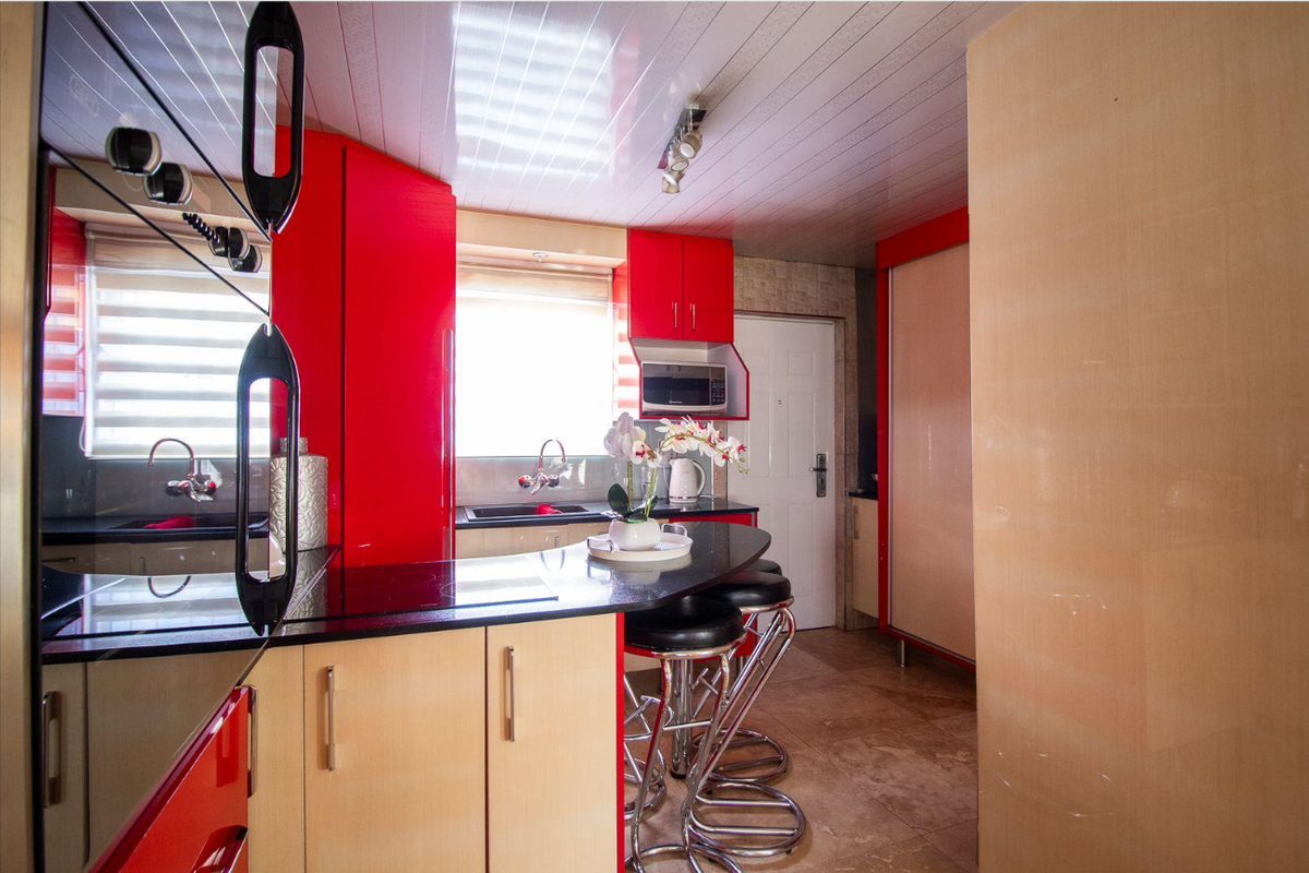 A vibrant kitchen featuring bold red cabinetry, black stone countertops, integrated appliances, and tiled flooring with a breakfast bar area.