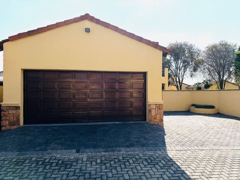 A well-maintained single garage featuring a dark wood-finish sectional door, stone-clad corner detailing, and a paved driveway.