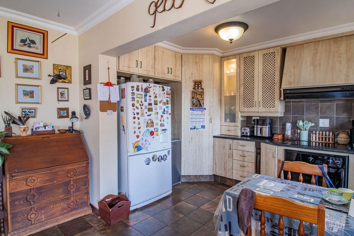 A functional kitchen featuring light wood-toned cabinetry, dark stone countertops, a built-in oven with extractor fan, and tiled flooring.