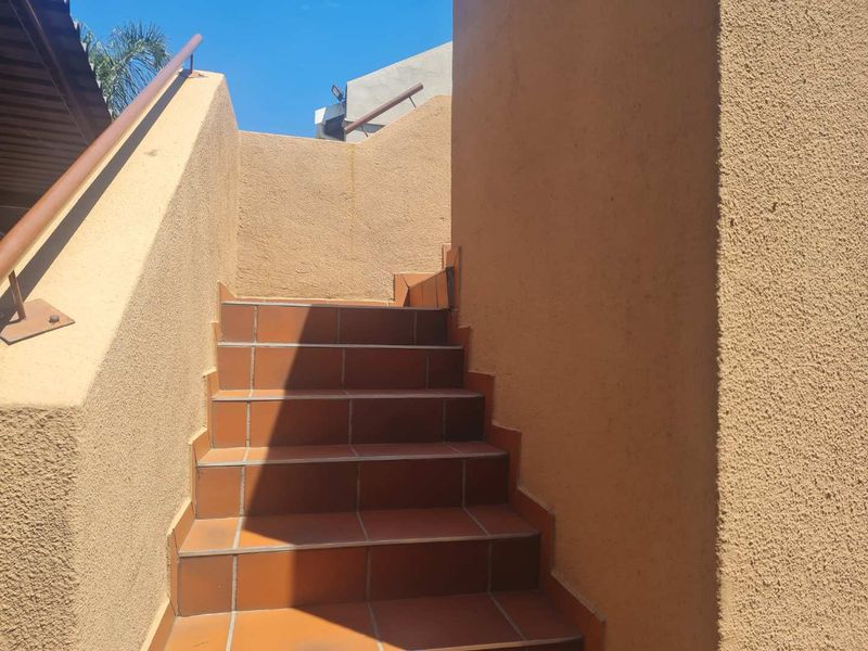 An exterior staircase featuring terracotta-style tiles and a metal handrail, leading to an upper level entrance.