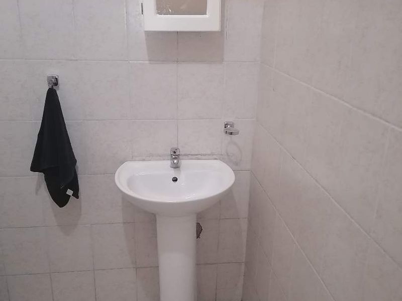 A functional bathroom featuring a white pedestal basin, wall-mounted medicine cabinet, and neutral ceramic tiling throughout.