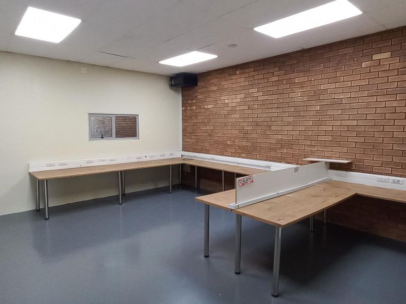 An industrial office space featuring exposed brick walls, durable flooring, and built-in workstation counters with integrated electrical trunking.