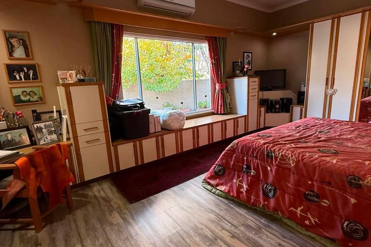 Spacious bedroom featuring built-in cabinetry, a window seat, ceiling fan, and split-system air conditioning, finished with modern laminate flooring.