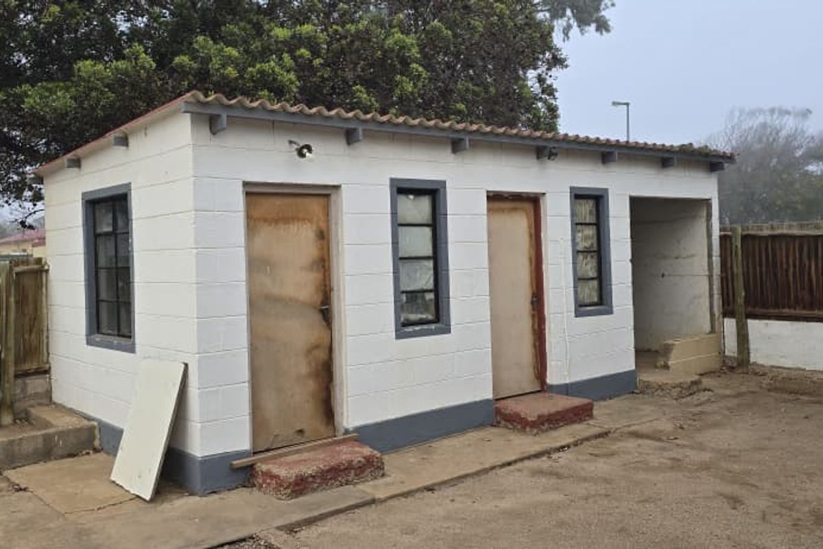 A detached outbuilding featuring multiple entry points, concrete block construction, and a corrugated roof, situated in a fenced backyard area.