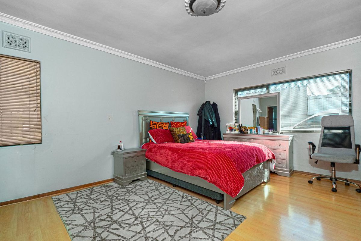 A spacious bedroom featuring laminate flooring, decorative cornice, and dual windows with integrated air vents, offering a functional and well-lit living space.
