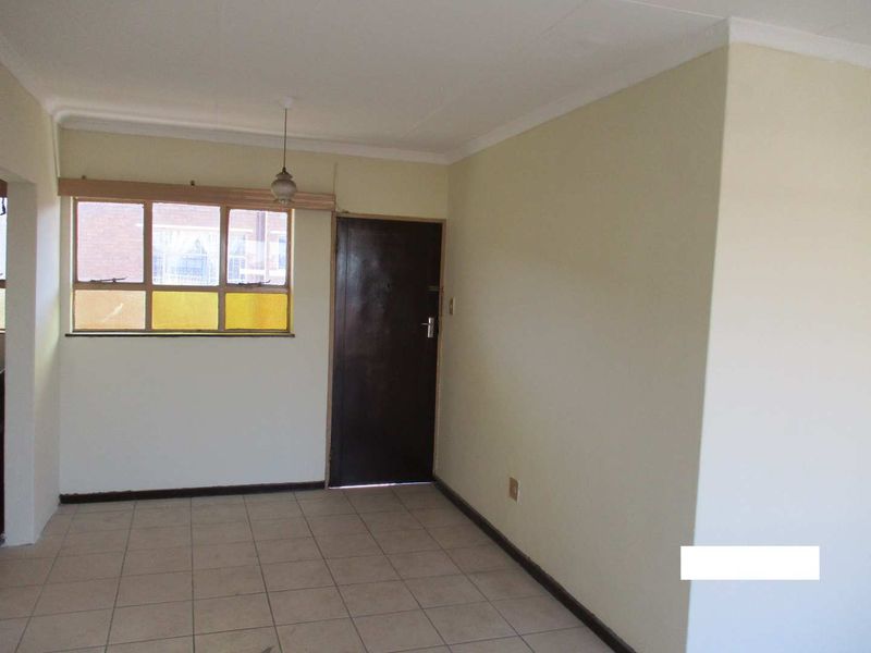 An empty living area featuring tiled flooring, a single-pane window, and a solid core door, offering a blank canvas for renovation.