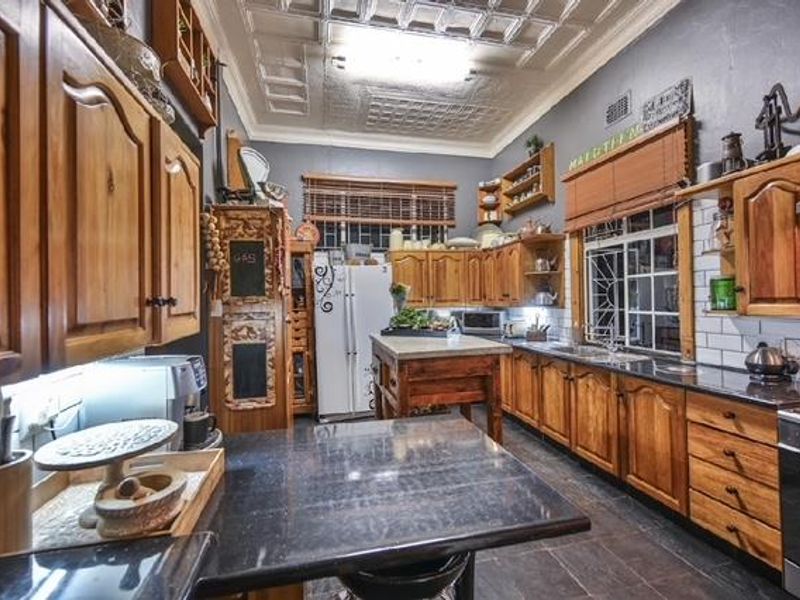 A traditional kitchen featuring timber cabinetry, granite countertops, a tiled splashback, and a distinctive pressed metal ceiling, offering a classic aesthetic.