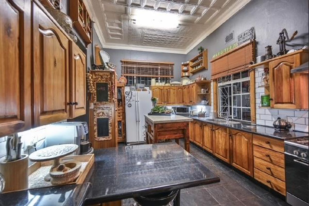 A traditional kitchen featuring timber cabinetry, granite countertops, a tiled splashback, and a distinctive pressed metal ceiling, offering a classic aesthetic.