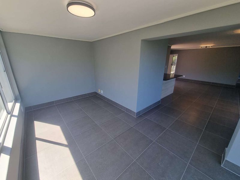 An open-plan living and kitchen area featuring modern grey floor tiles, neutral wall tones, and a kitchen island with a granite countertop.