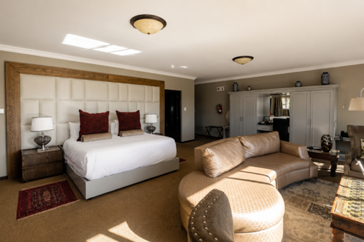 Spacious bedroom suite featuring a large upholstered headboard, built-in cabinetry, and a comfortable seating area with neutral wall finishes and carpeted flooring.
