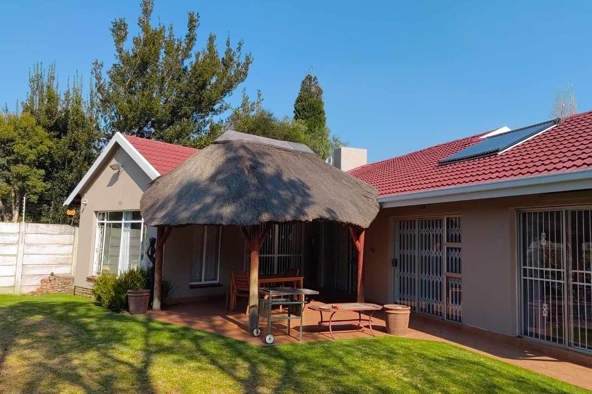 Rear view of the house featuring a paved patio with a thatched lapa, solar water heating panels, and secure sliding door access.