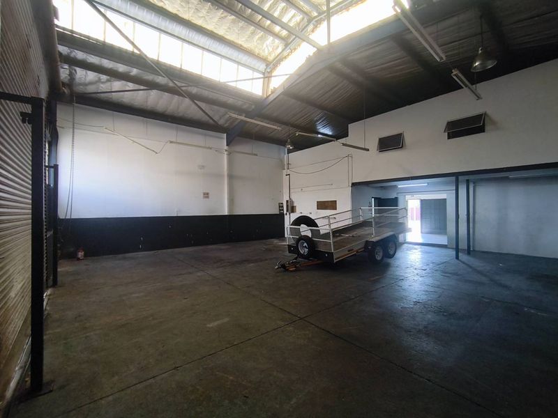 Spacious industrial utility area featuring high-clearance ceilings, natural light from skylights, and durable concrete flooring, suitable for various commercial or storage applications.