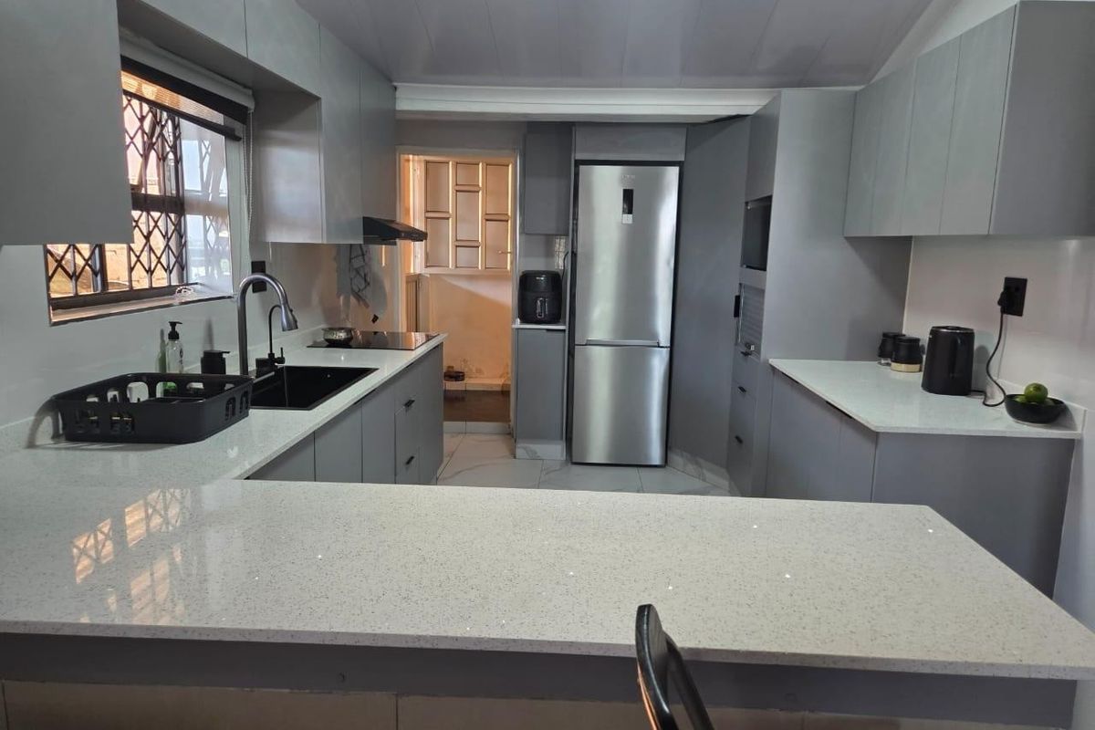 Modern kitchen featuring sleek grey cabinetry, quartz countertops, integrated appliances, and a breakfast bar, offering a clean and functional culinary space.