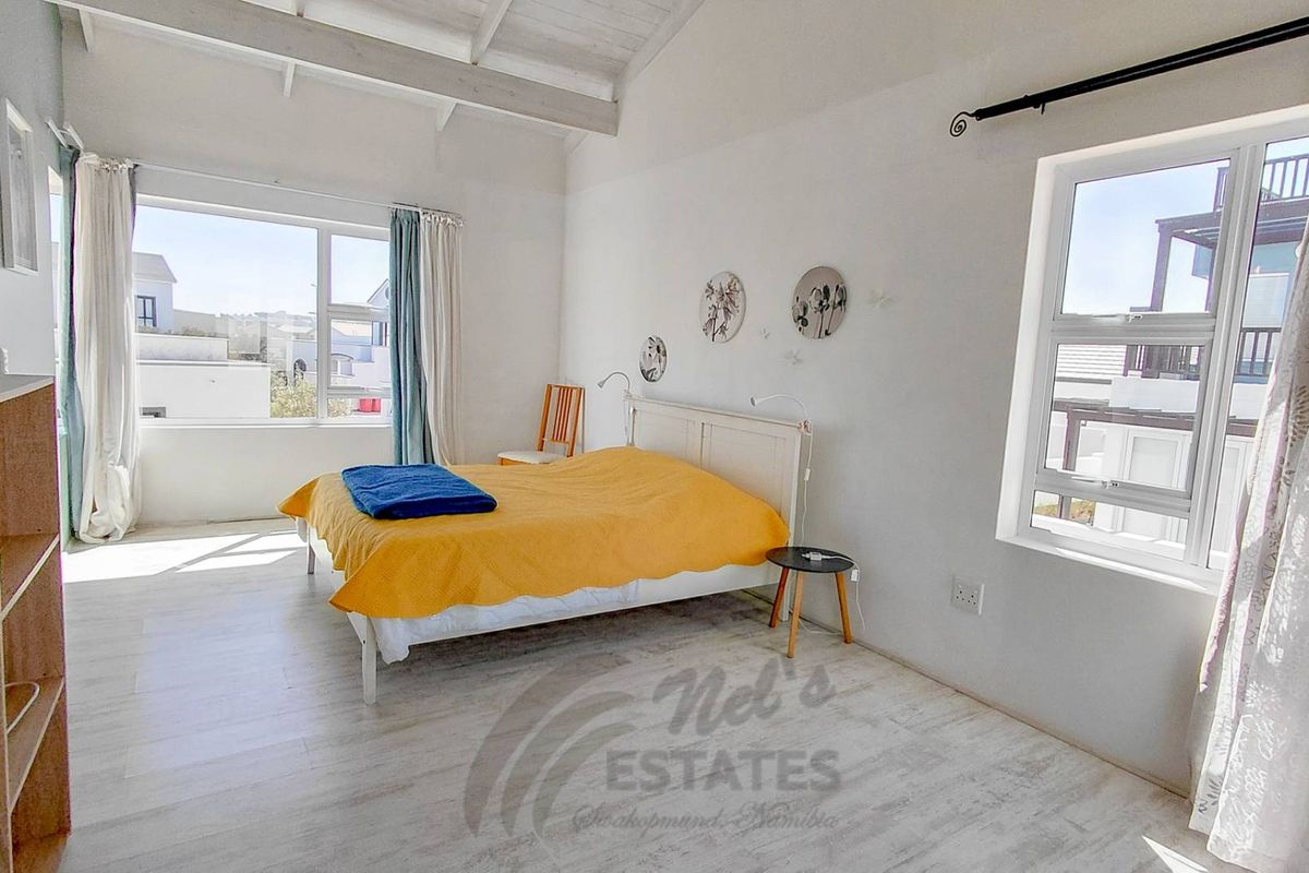 A bright bedroom featuring vaulted ceilings, light-toned flooring, and large windows that provide ample natural light.