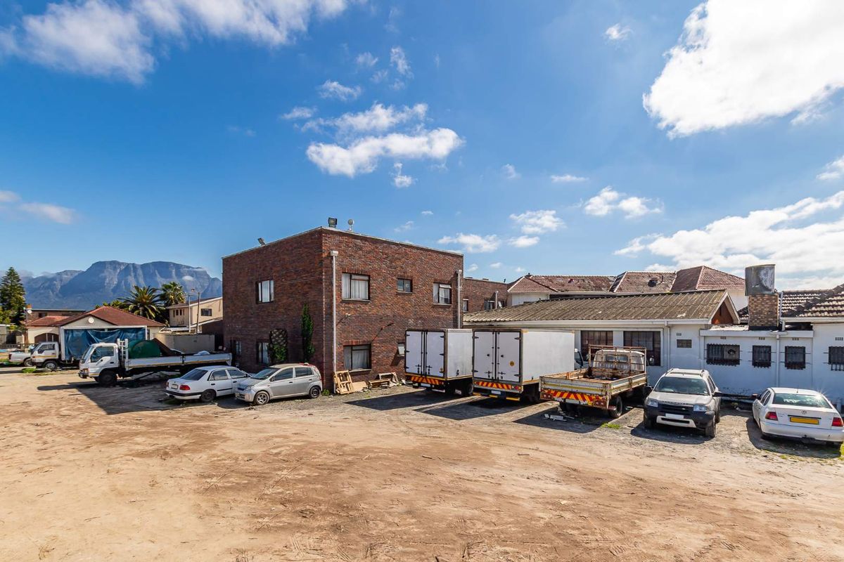 Exterior view of a mixed-use property featuring a brick building and adjacent structures with a large unpaved yard area.