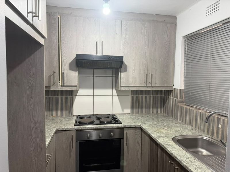 Compact kitchen featuring wood-look cabinetry, granite countertops, built-in oven, electric hob, and a stainless steel sink with tiled backsplash.