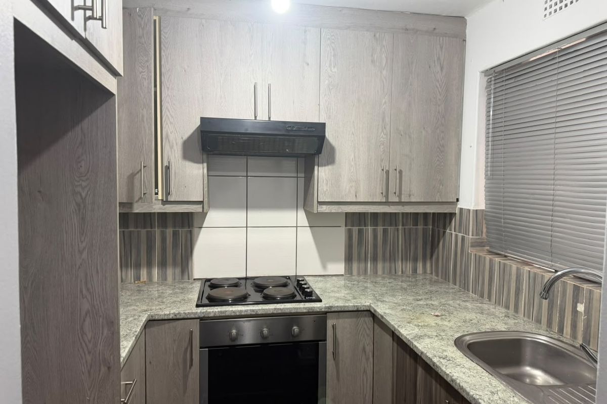Compact kitchen featuring wood-look cabinetry, granite countertops, built-in oven, electric hob, and a stainless steel sink with tiled backsplash.