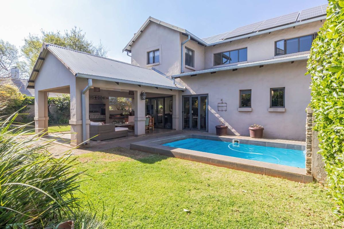Rear view of the property featuring a covered patio with built-in braai, a swimming pool, and solar panels on the roof.