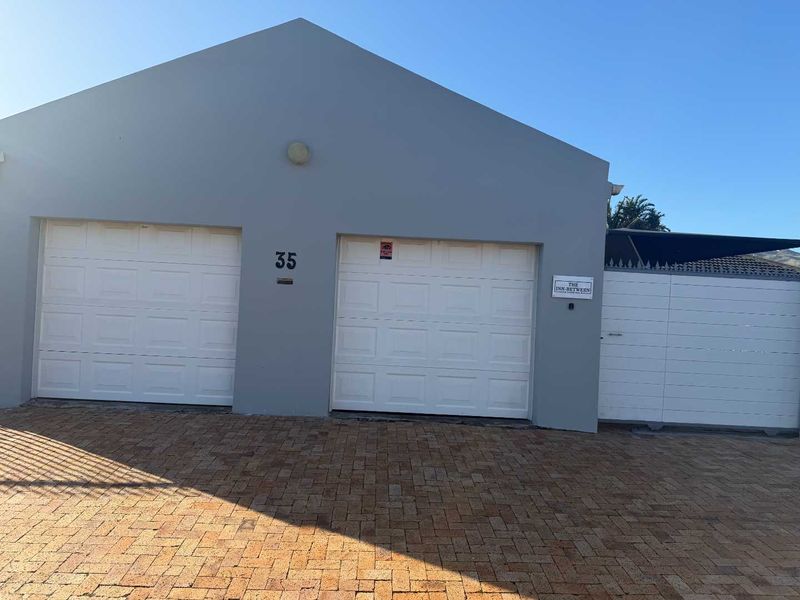 Front elevation of the property featuring a double garage with white sectional doors and a paved driveway entrance.