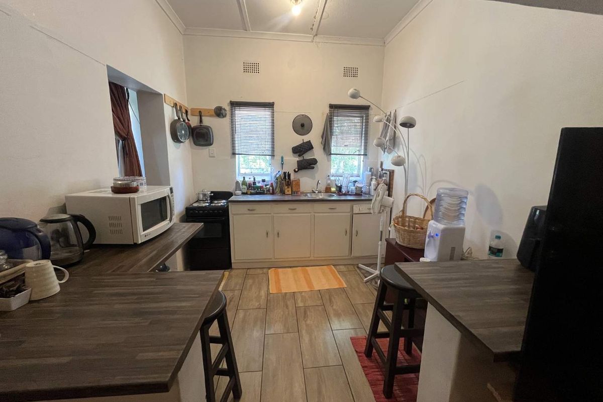 A functional kitchen featuring wood-look laminate countertops, built-in cabinetry, a stainless steel sink, and tiled flooring with a freestanding stove.