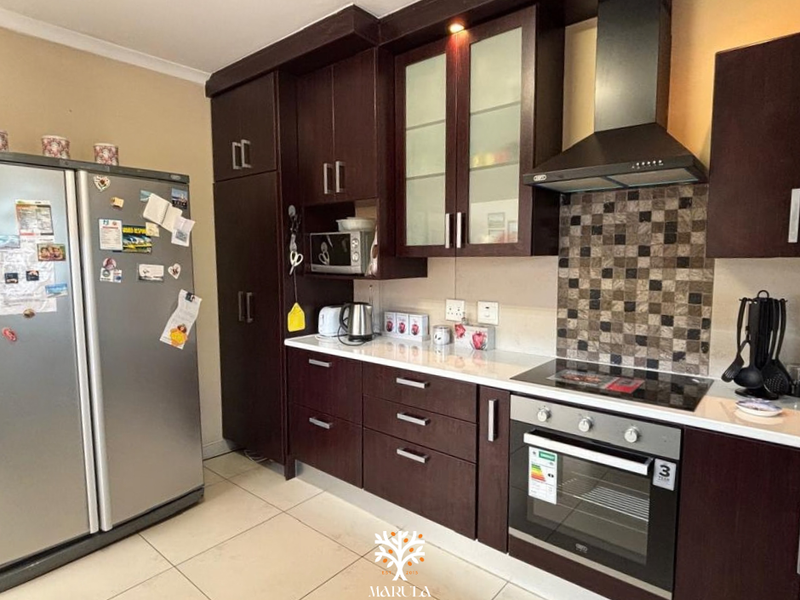 Modern kitchen featuring dark wood cabinetry, stone countertops, mosaic tile backsplash, and integrated stainless steel appliances including an oven and extractor fan.