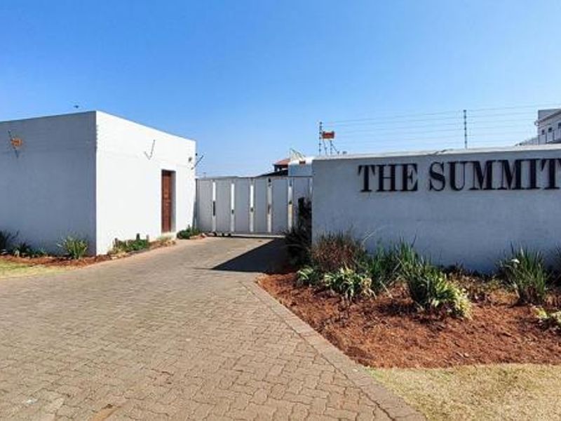 The entrance to The Summit complex featuring a paved driveway, security gate, and perimeter boundary wall with electric fencing.