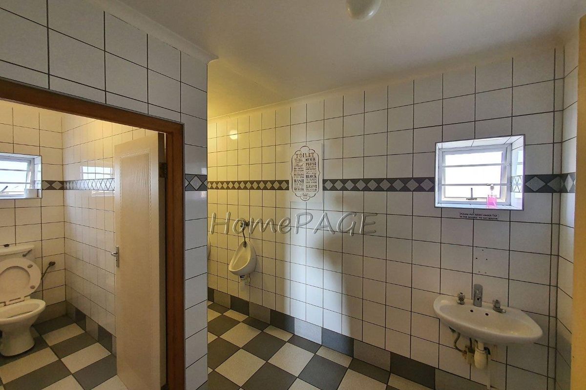 A functional commercial restroom facility featuring tiled walls, a wall-mounted basin, and a separate toilet cubicle with a urinal area.