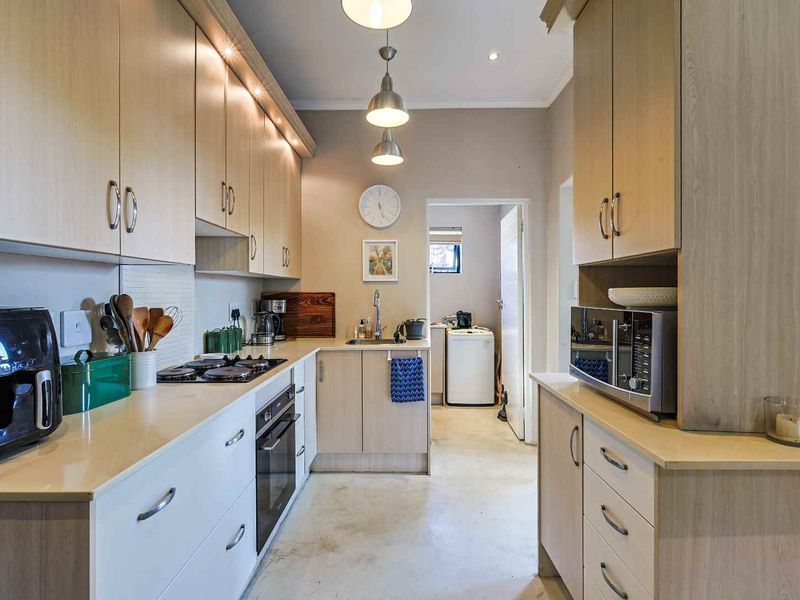 A well-lit kitchen featuring light wood cabinetry, a gas hob, built-in oven, and a functional layout with an adjacent laundry area.
