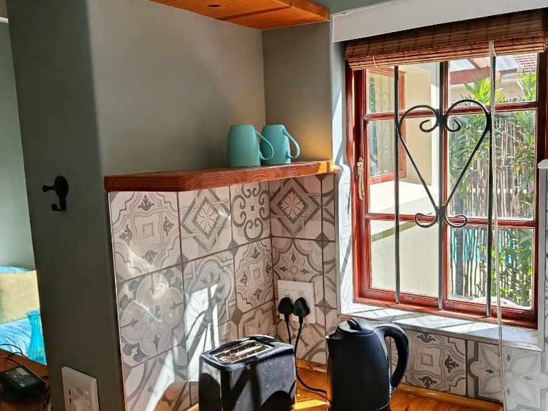 A cozy kitchen corner featuring a polished timber countertop, decorative patterned splashback tiles, and timber floating shelving with natural light.