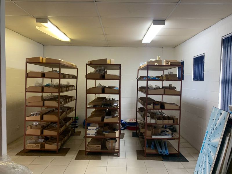 A functional utility or storage space featuring tiled flooring, drop ceiling, and fluorescent lighting, currently utilized for organized shelving and inventory storage.