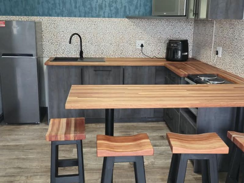 Modern kitchen featuring dark grey cabinetry, warm wooden countertops, a tiled backsplash, and a breakfast bar area with integrated sink and faucet.