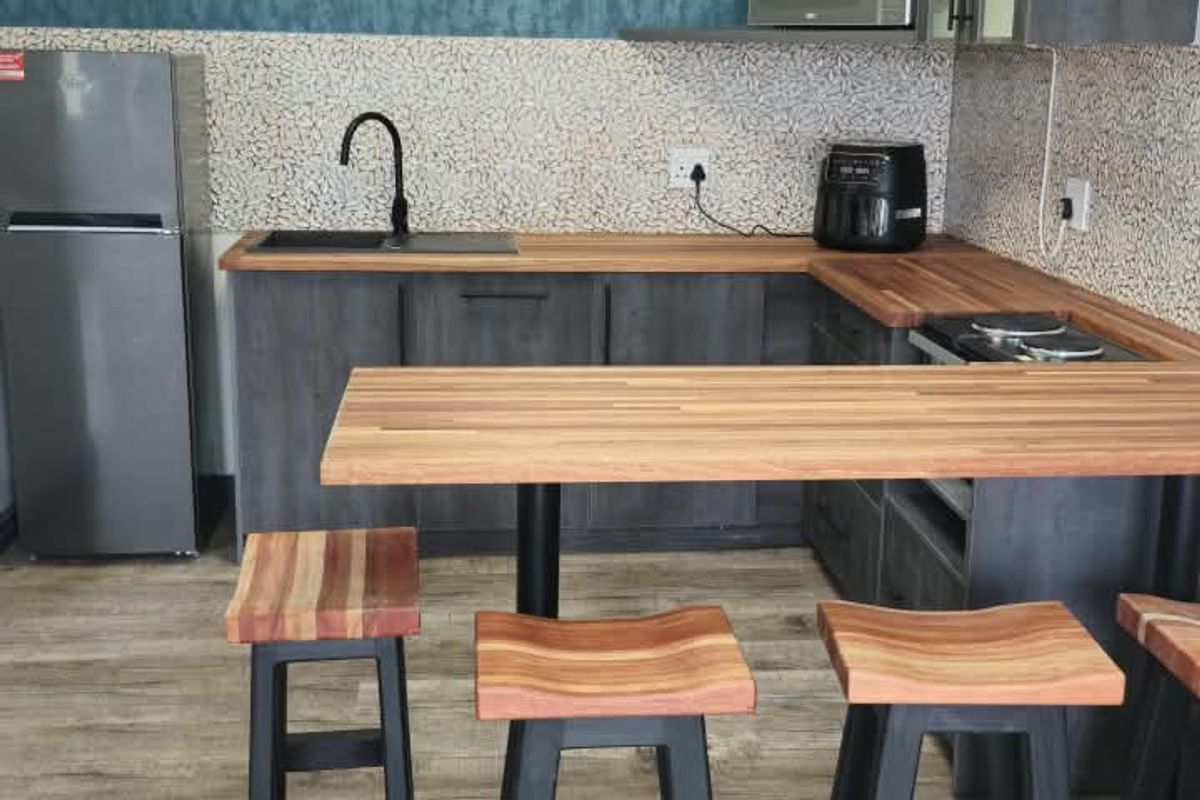 Modern kitchen featuring dark grey cabinetry, warm wooden countertops, a tiled backsplash, and a breakfast bar area with integrated sink and faucet.