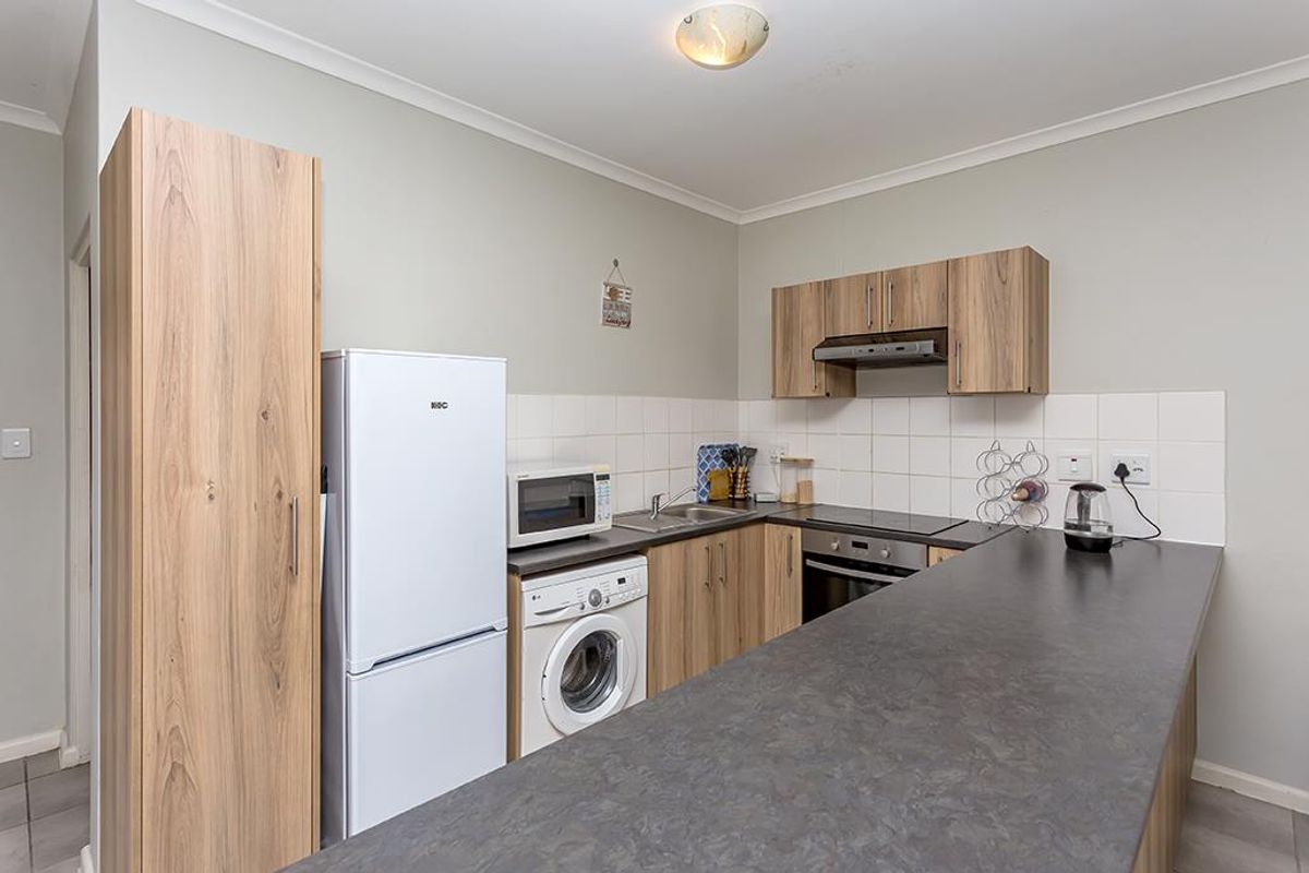 Functional kitchen featuring wood-look cabinetry, dark laminate countertops, built-in oven, electric hob, extractor fan, and tiled splashback.