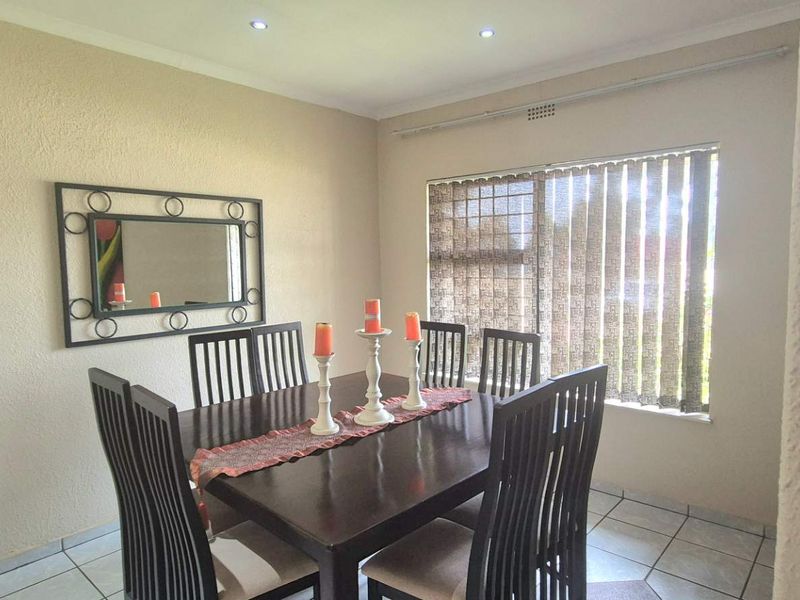 A functional dining room featuring tiled flooring, recessed downlighting, and a large window fitted with vertical blinds and security bars.