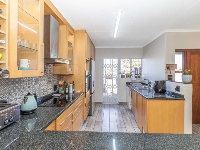 Functional kitchen featuring light wood cabinetry, granite countertops, patterned backsplash, and direct access to the exterior via a security gate.