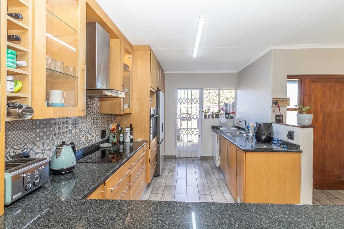 Functional kitchen featuring light wood cabinetry, granite countertops, patterned backsplash, and direct access to the exterior via a security gate.