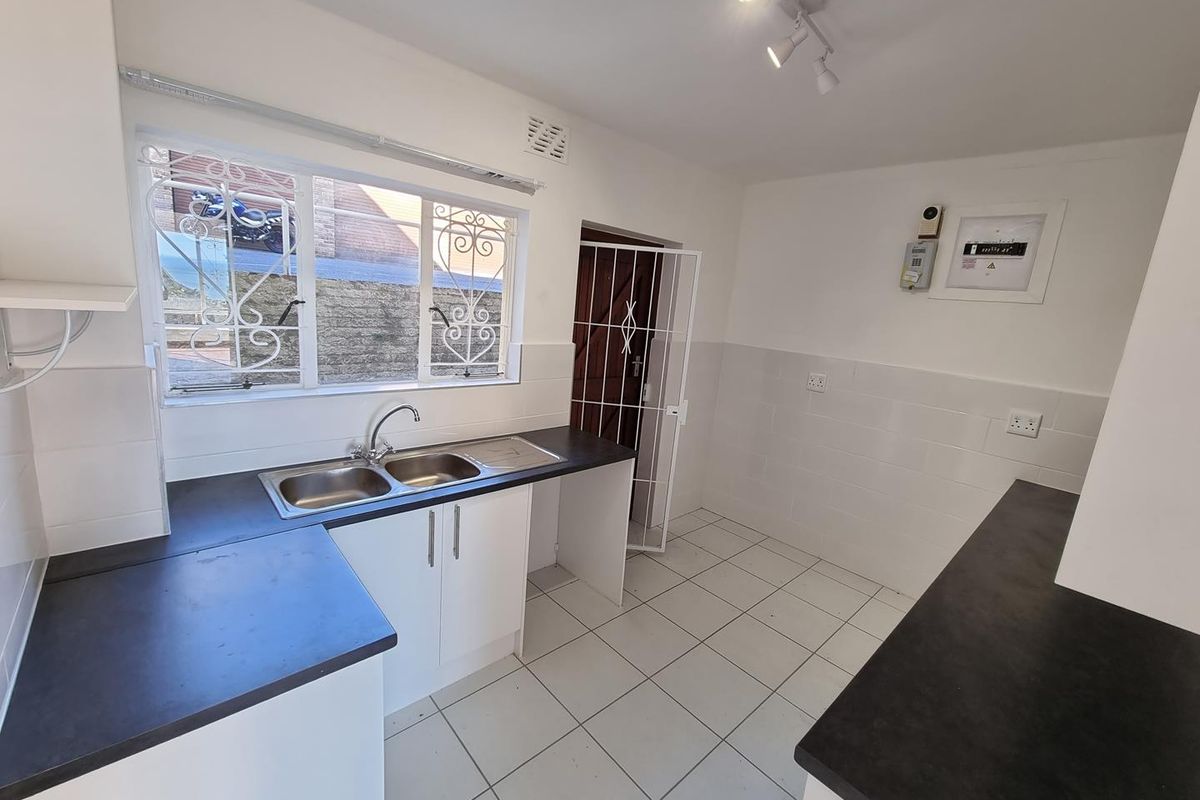 A functional kitchen featuring white cabinetry, dark countertops, a double-basin sink, and tiled flooring with security gate access.