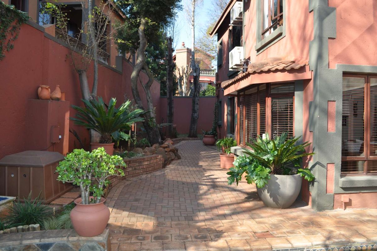 A paved rear courtyard area featuring established landscaping, brick retaining walls, and direct access to the home's exterior facade.