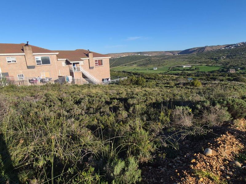 A view of the vacant residential land featuring natural vegetation with adjacent residential buildings and a scenic landscape backdrop.