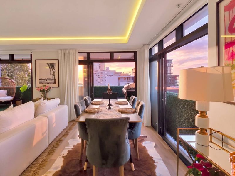 Bright open-plan living and dining area featuring modern recessed ceiling lighting, large sliding glass doors, and seamless access to an outdoor balcony.