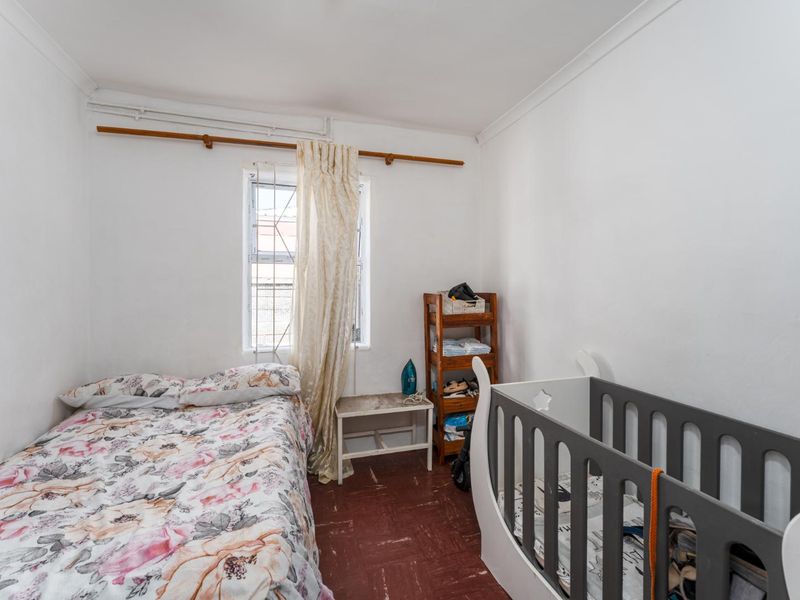 A compact bedroom featuring a window with a curtain rod and dated flooring, offering a functional space ready for modernization.