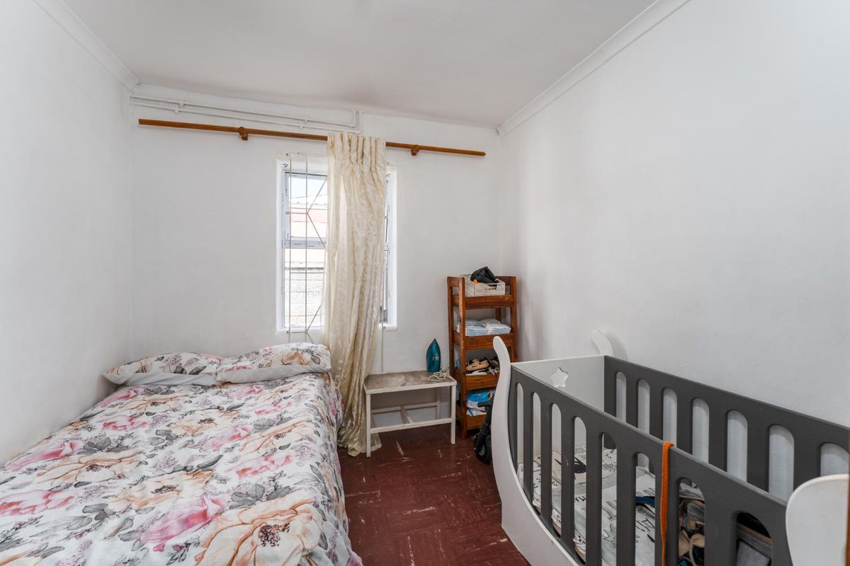 A compact bedroom featuring a window with a curtain rod and dated flooring, offering a functional space ready for modernization.